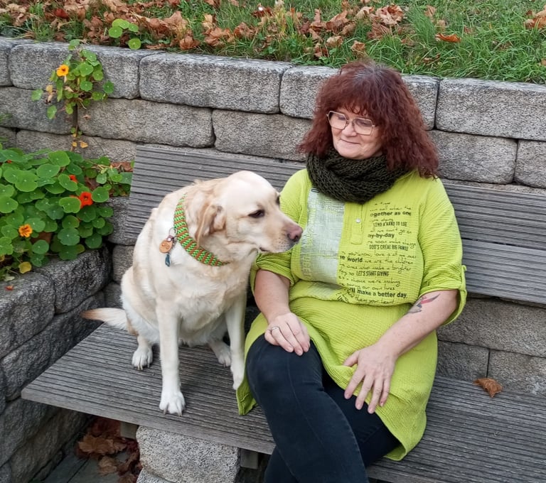 Carmen sitzt mit ihrer Labradorhündin Bonny auf einer Bank.