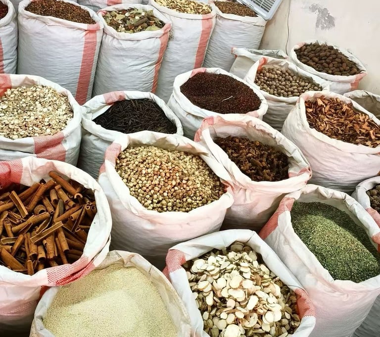 Large white sacks filled with various bulk spices, dried herbs, and roots in an open-air market stall.
