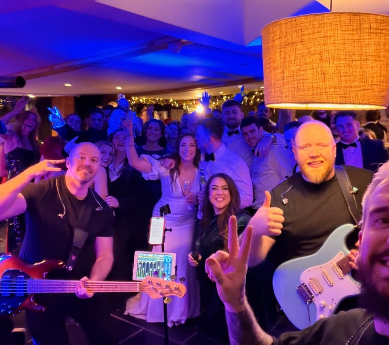 A professional live wedding band performs for a cheering crowd at a lively indoor reception.