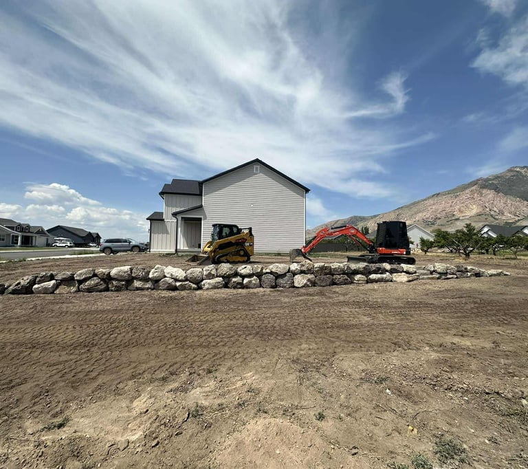 Boulder retaining wall with skid steer and mini excavator sitting idle