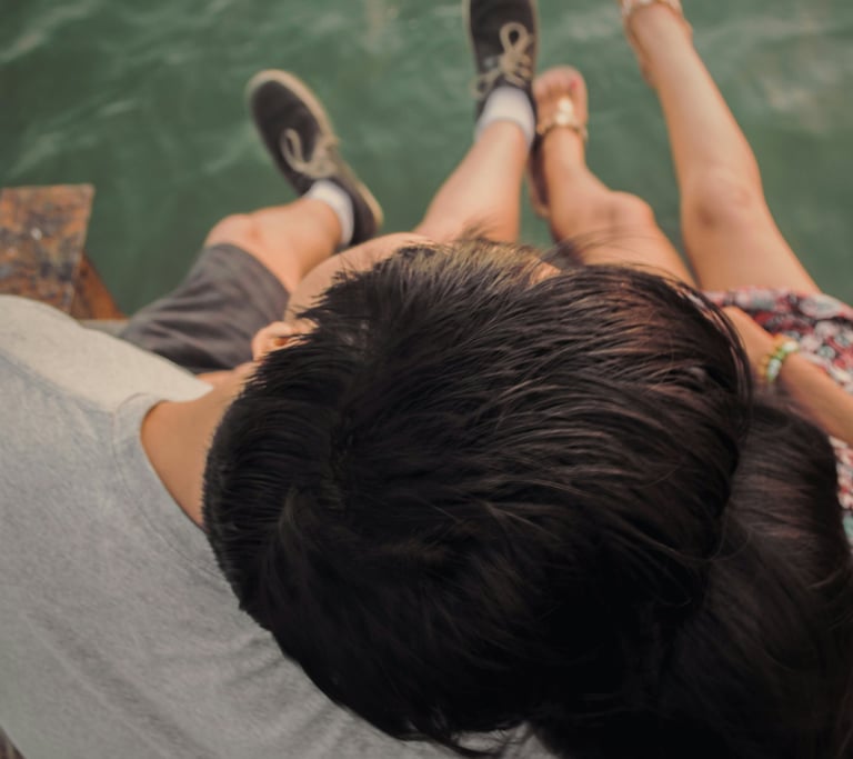 Couple enlacé, vu du dessus, assis sur un ponton en bois, les jambes au dessus de l'eau..