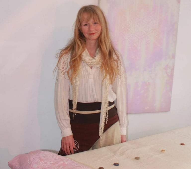 Reiki practitioner smiling in a calm healing room with a treatment table and pastel artwork