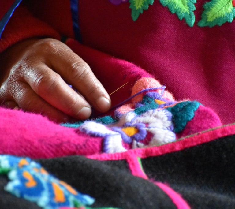 mano de una artesana con una aguja bordando una flor en un paño rosado