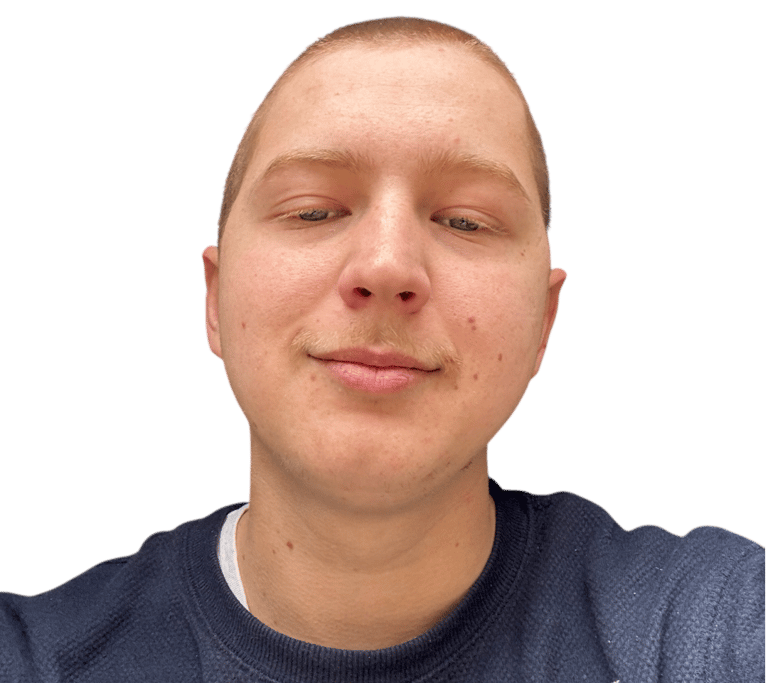 Smiling young man with a buzz cut and mustache wearing a blue sweater against a black background.