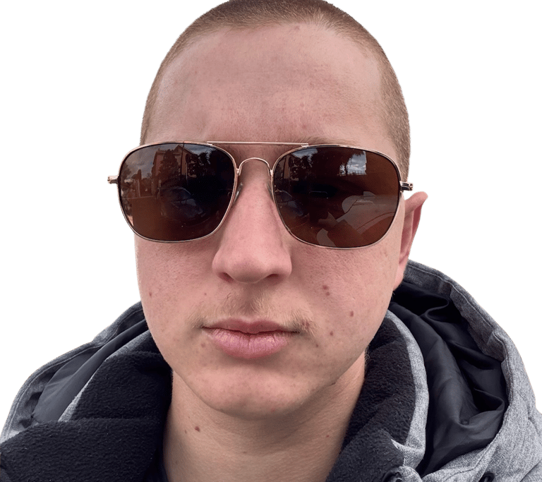 Portrait of a man with a buzz cut wearing gold aviator sunglasses and a grey hooded jacket.