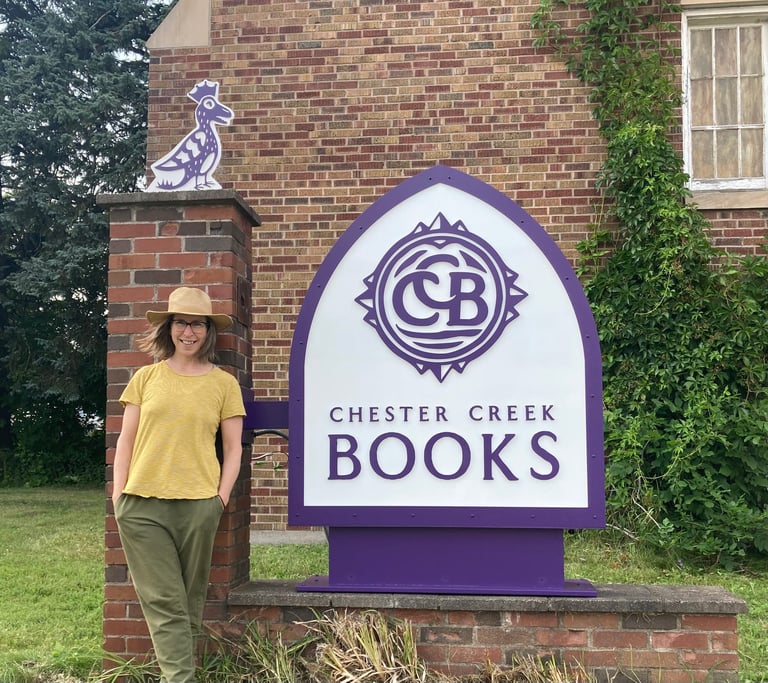 Owner Tina standing in front of purple and white Chester Creek Books sign