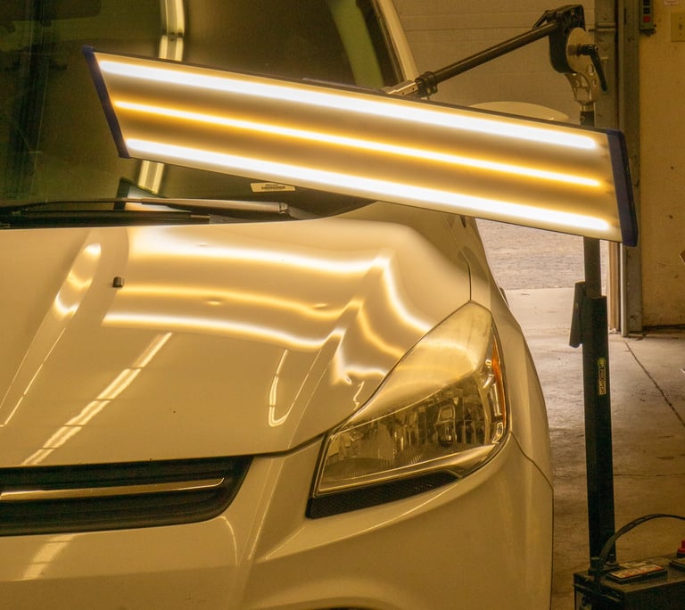 Hail damage on the hood of a white car, shown by the special LED PDR light.