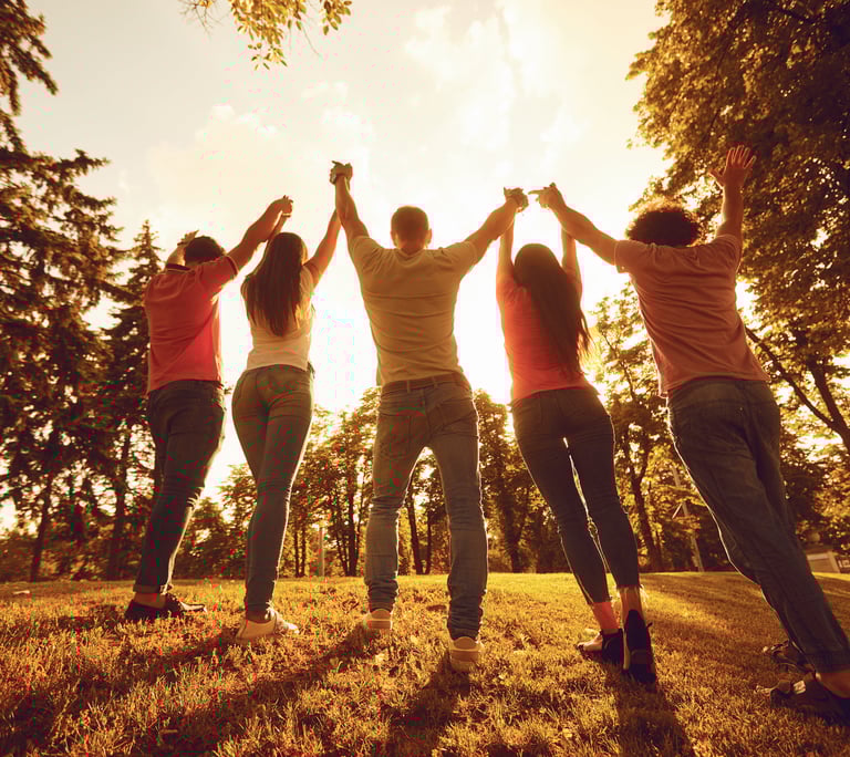 Groupe uni dans un geste de célébration, les bras levés vers le ciel, au coucher du soleil