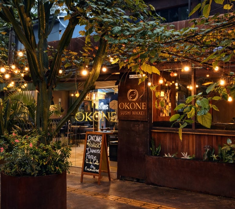 Fachada iluminada do restaurante Okone em São Paulo, destacando a área externa com mesas, luzes decorativas e paisagismo