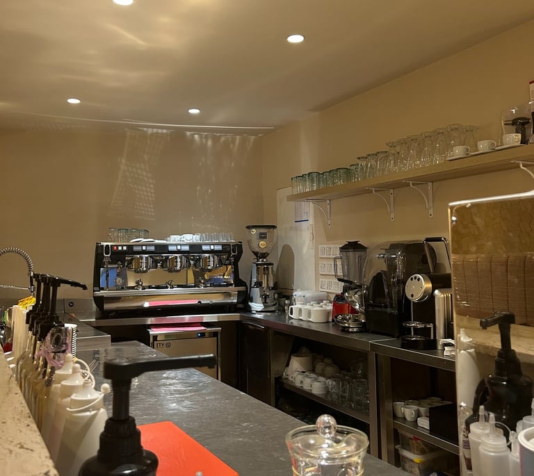 Professional coffee bar setup featuring a stainless steel espresso machine, grinders, and syrup dispensers.