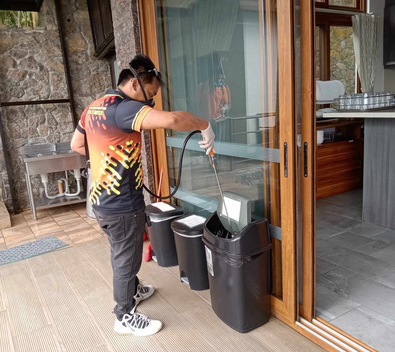 Professional pest control technician spraying disinfectant into outdoor trash cans for sanitation.