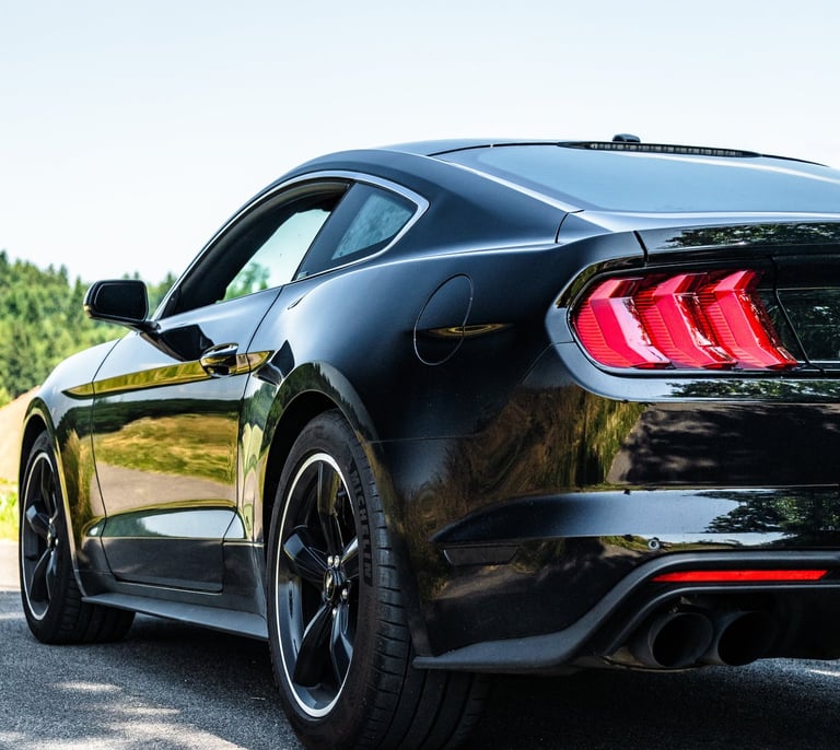 Schwarzer Ford Mustang auf Landstraße, tief fotografiert, zeigt Rückleuchten, Felgen 