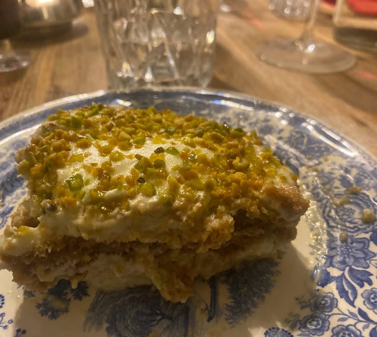 Slice of creamy pistachio tiramisu dessert topped with crushed nuts on a blue floral plate.