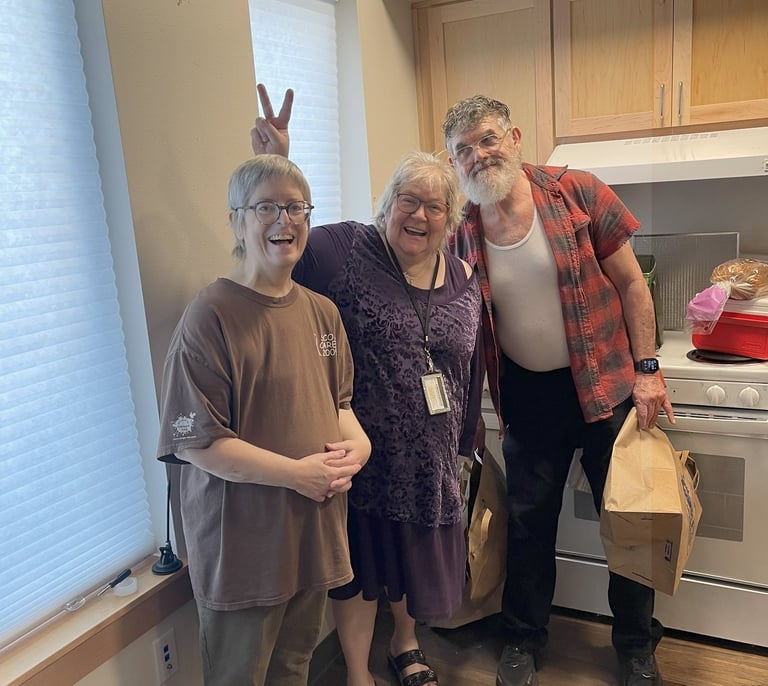 Three seniors stand together in an apartment smiling, one of them is holding up bunny ears