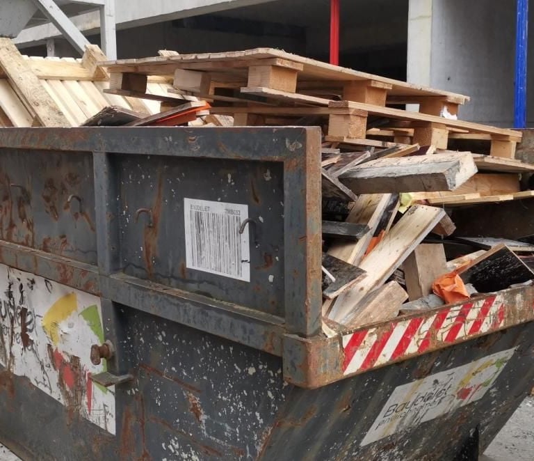 Benne de chantier remplie de bois et matériaux divers issus de travaux de démolition ou rénovation.