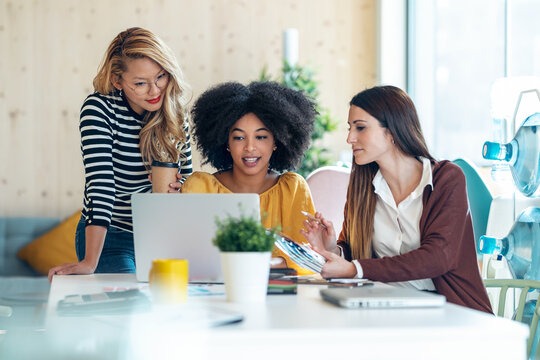 three women sitting at a table viewing a laptop