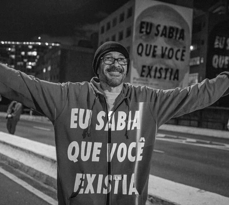 Homem com braços abertos e texto projetado no peito "eu sabia que você existia"