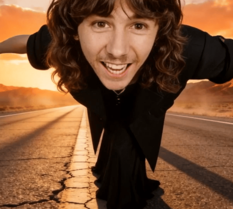 Smiling man with long hair Jimi Nix posing on a desert road at sunset with arms outstretched.