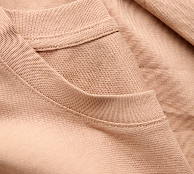 Close-up of a beige crew neck t-shirt showing the ribbed neckline and soft cotton jersey fabric texture.