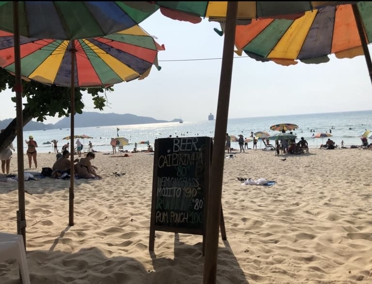 Sonniger Patong Beach in Phuket mit bunten Sonnenschirmen und einer Getränkekarte im Sand
