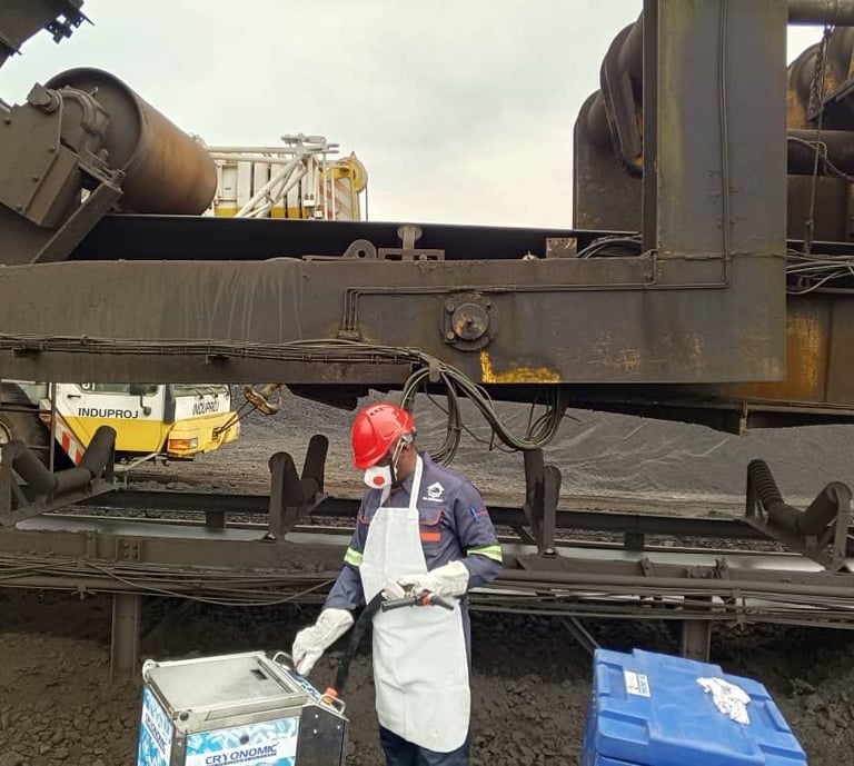 Industrial technician in safety gear performing dry ice blasting on heavy mining machinery.