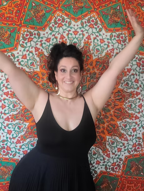 Image of Maria with her hands up with a big smile. The background is a orange and green mandala.