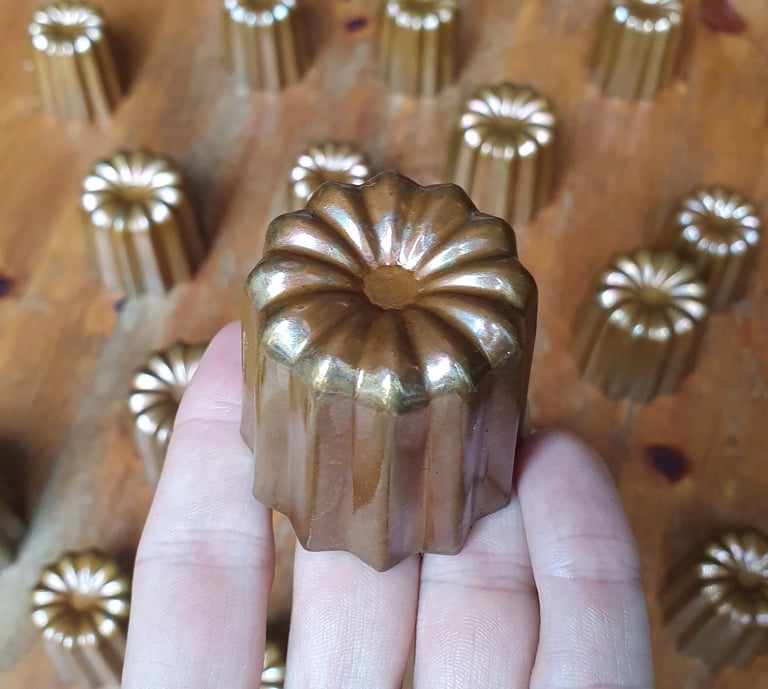 Un moule à cannelé en cuivre tenu dans une main