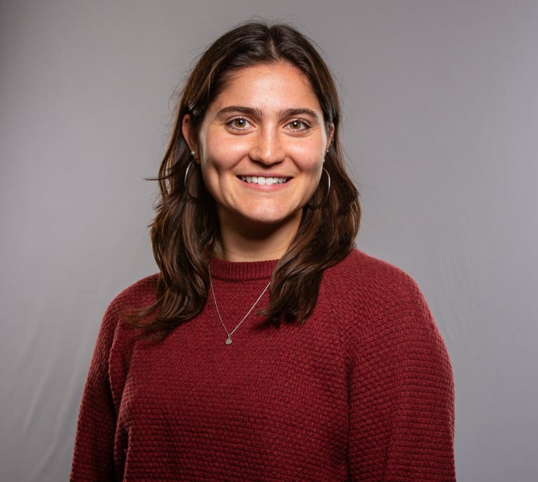 Professional headshot of a smiling woman with brown hair wearing a maroon sweater against a grey background.