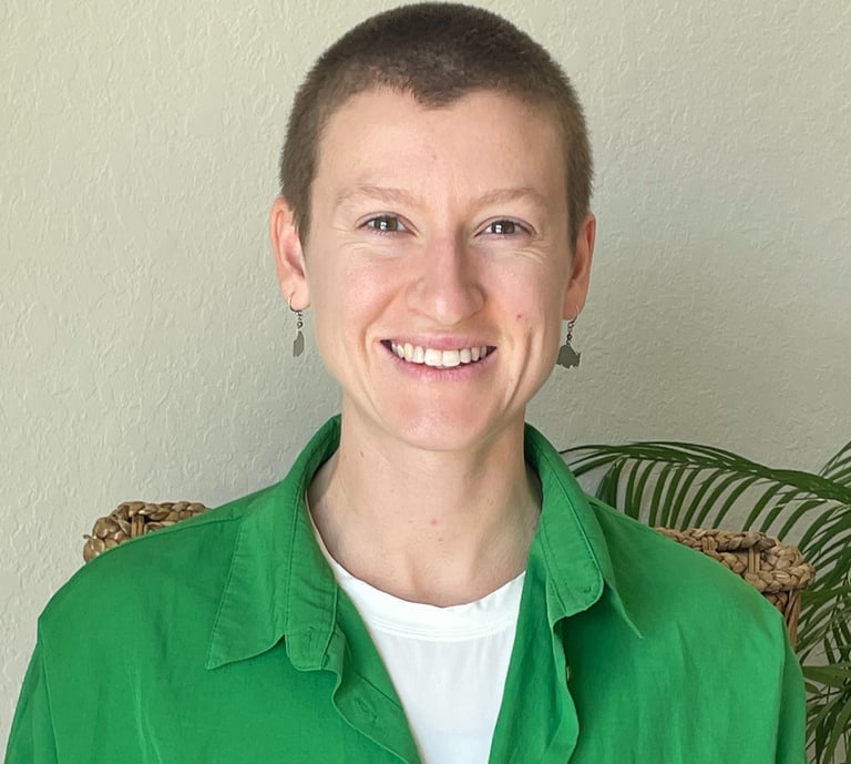 Smiling woman with a buzz cut wearing a green button-down shirt and dangling earrings.