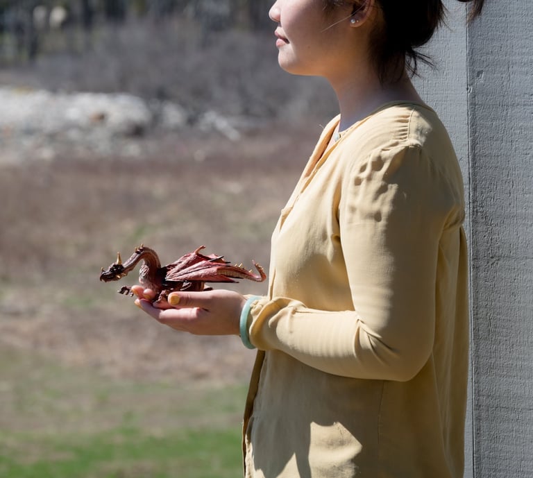 Side profile of a woman holding a small red toy dragon figurine outdoors on a sunny day.
