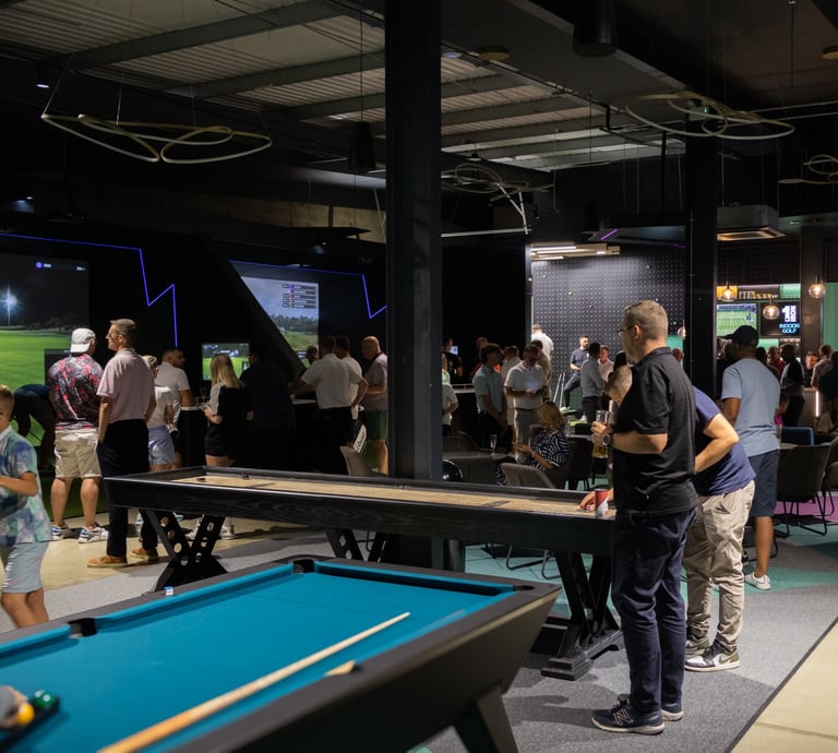 A busy event at 1IRON indoor golf simulator venue with people playing pool, shuffleboard and golf