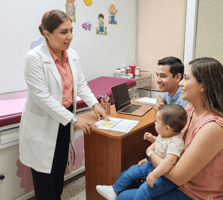 Una pediatra con bata blanca consulta con unos padres y su bebé en una clínica médica.