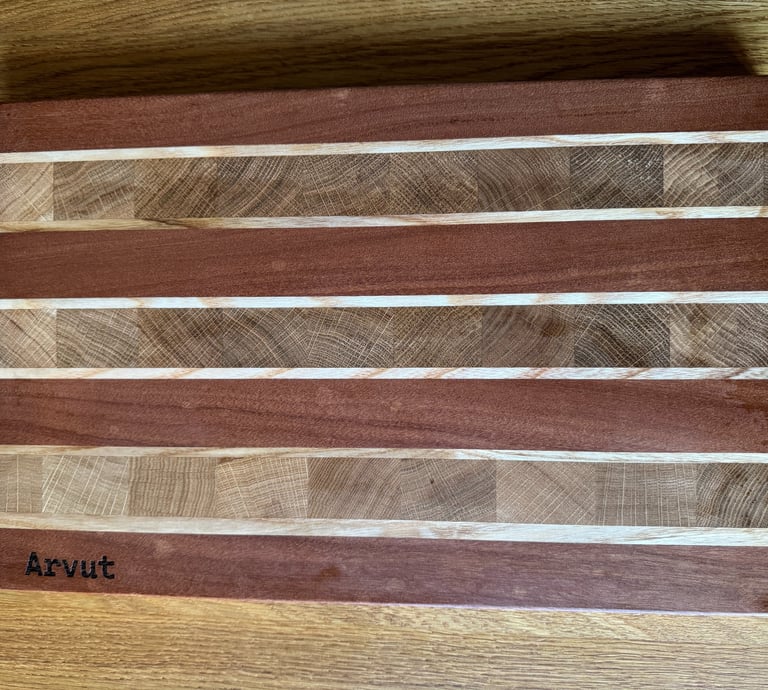 Handmade wooden cutting board with a striped pattern of mahogany and maple wood grain on a table.