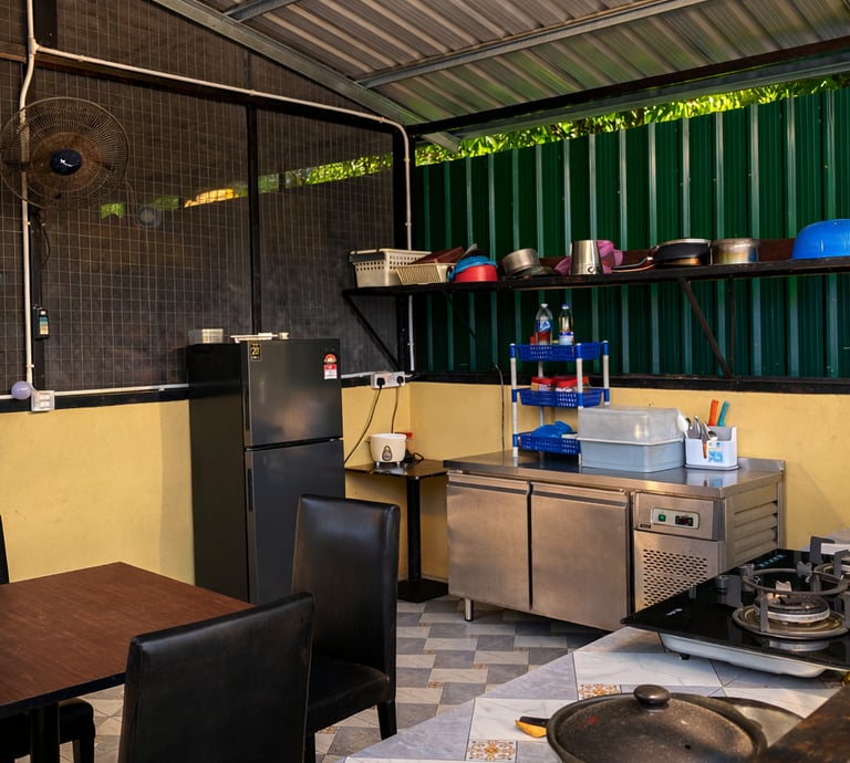 An outdoor commercial kitchen area featuring a stainless steel prep table, gas stove, and refrigerator.