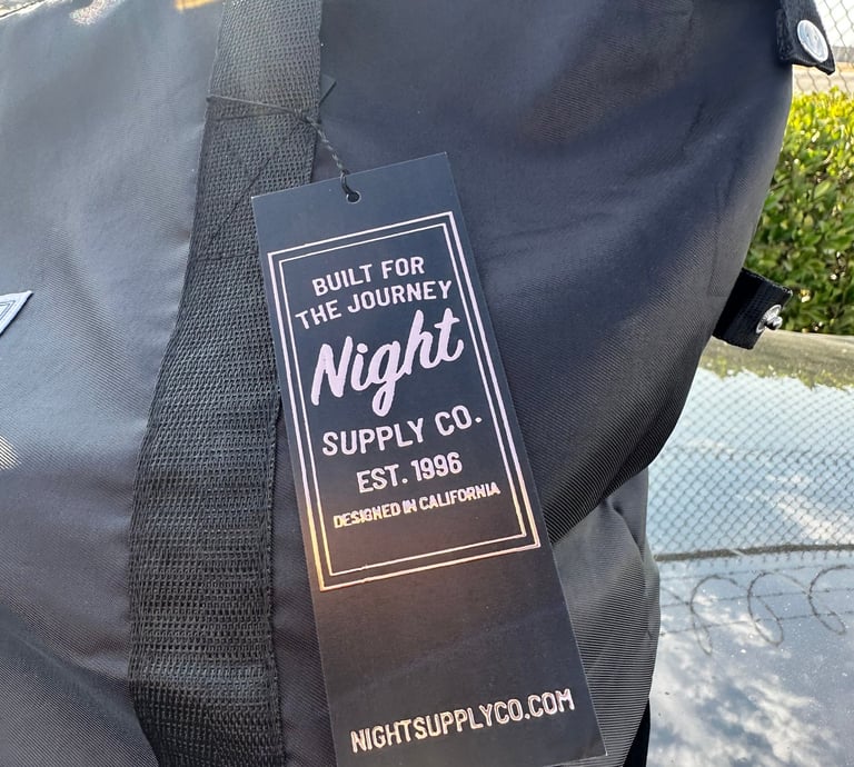 Black Night Supply Co. duffel bag with woven handle and branded hang tag