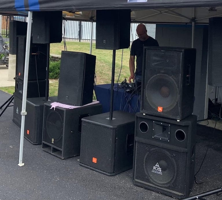 man under a tent behind speakers playing music