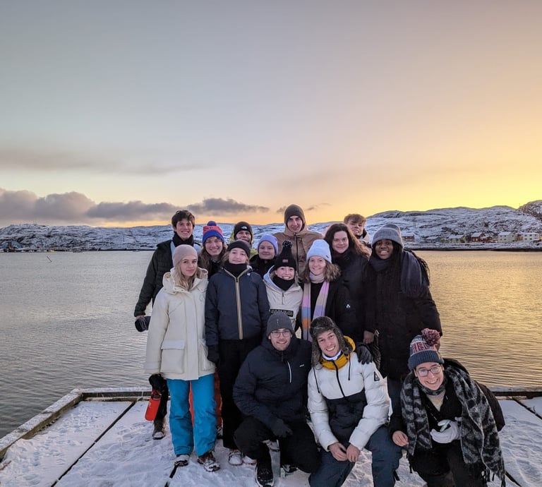 a group of people standing on a dock with a boat and beautiful sunset in the Nordic background