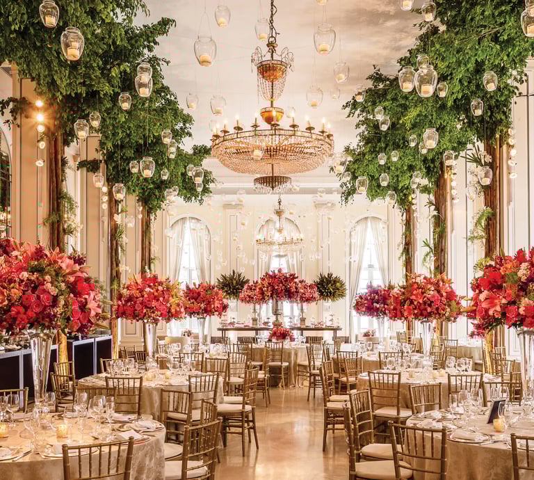 Elegant luxury wedding reception ballroom with pink floral centerpieces, crystal chandeliers, and indoor trees.