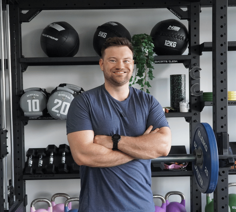 Lächelnder Personal Trainer in Bielefeld posiert im Fitnessstudio mit Kurzhanteln, Kettlebells