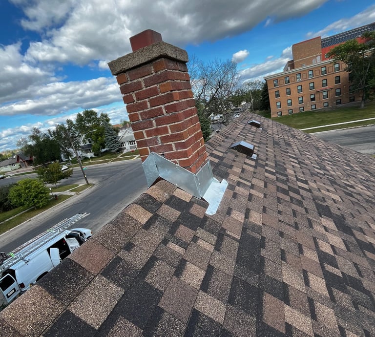 Gabled roof peak, brown asphalt shingles and chimney flashing. Roof vents and brick chimney. 