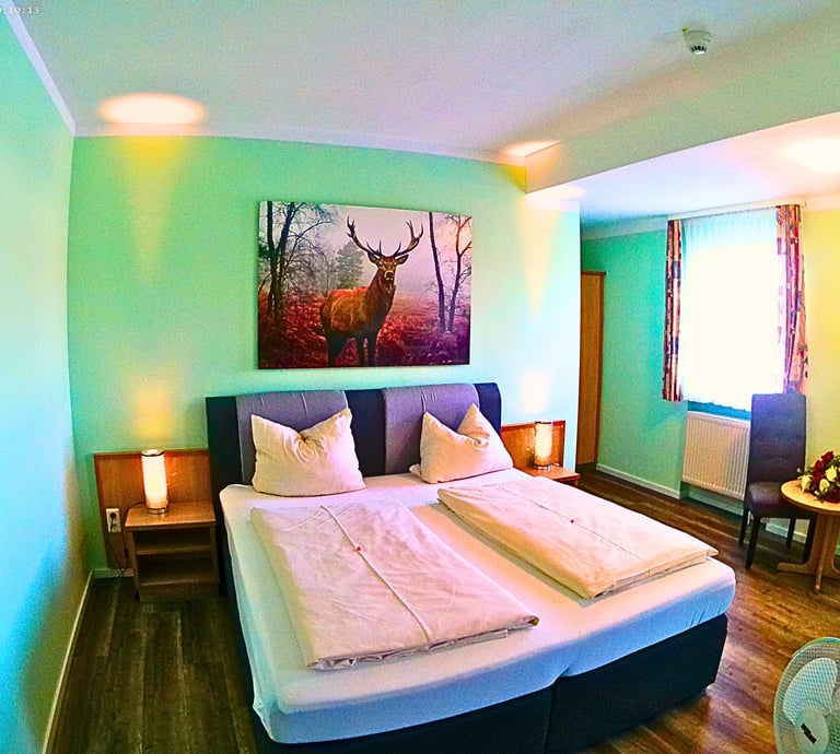 Cozy hotel room with a double bed, mint green walls, and a large stag painting above the headboard.