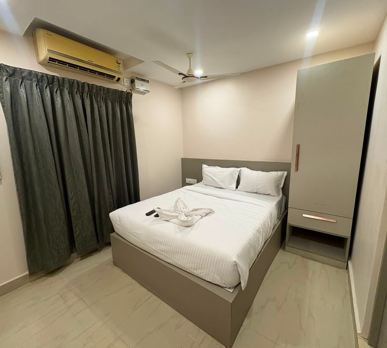 Modern budget hotel room with white double bed, gray wardrobe, air conditioning, and dark curtains.