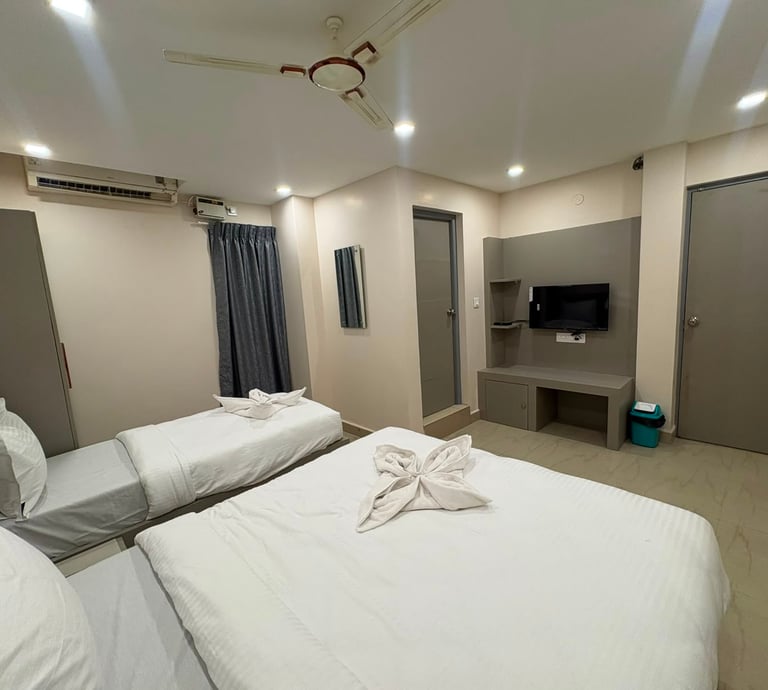 Modern hotel room with double and single beds, white linens, wall-mounted TV, and ceiling fan.