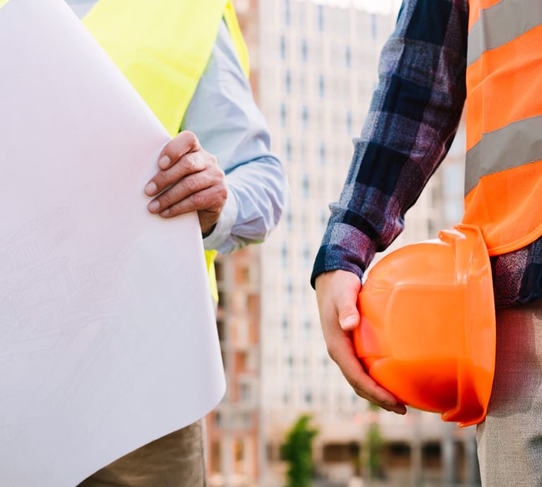 Dupla de construtores onde vemos um com um capacate na mão e outro segurando um projeto