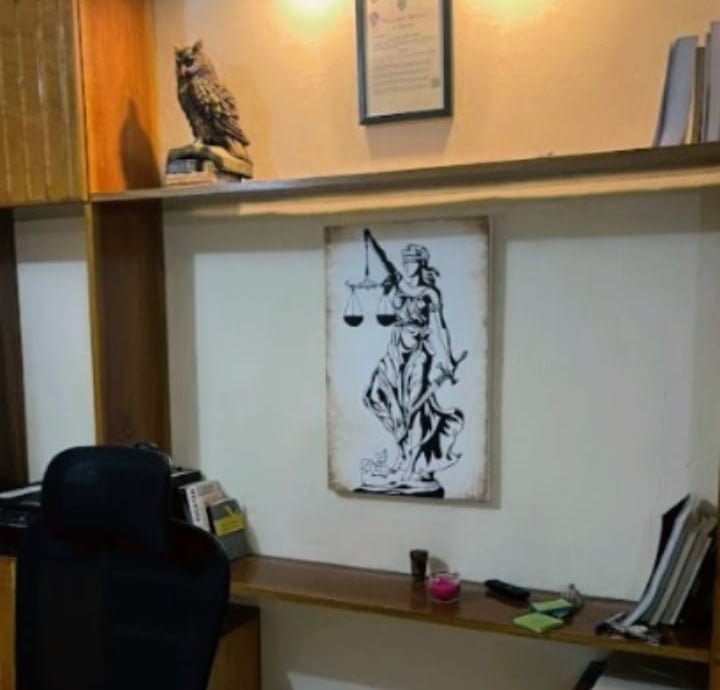 Pared blanca de oficina con repisas. Un diploma, un cuadro decorativo alusivo a la justicia y un buho