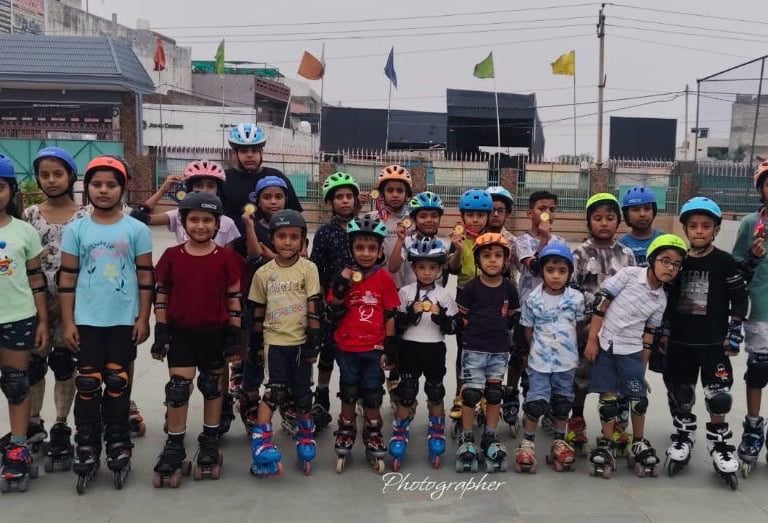 Group of young children wearing helmets and pads during a roller skating class outdoors.