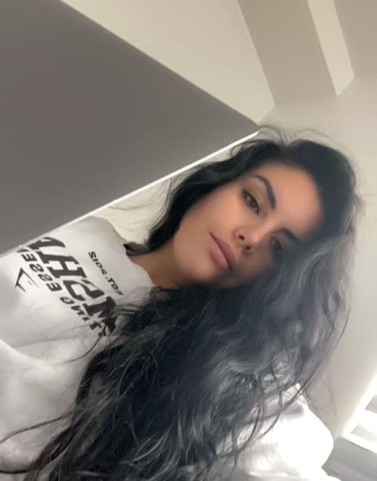 Young woman with long dark wavy hair wearing a white sweatshirt looking at a laptop computer.