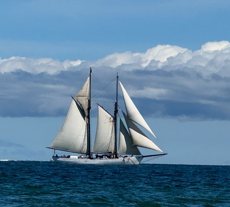 A classic two-masted schooner sailing on blue ocean water under a cloudy sky.