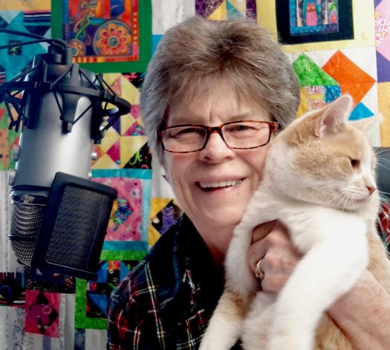 Diane Lalomia, the artist  is holding her cat, Honey with a quilt top with cats & dogs, Diane pieced