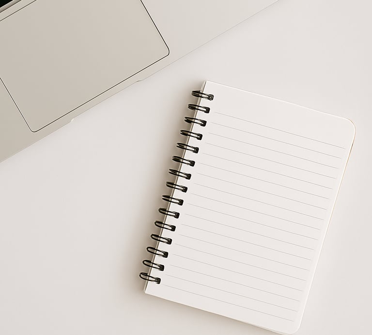 Minimalist home office setup with a silver laptop, open blank spiral notebook, and white desk for productivity and work.